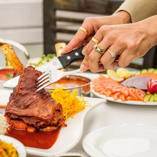 Hands cutting into a large Indian lamb shank with a knife and fork, served with sauce and rice.