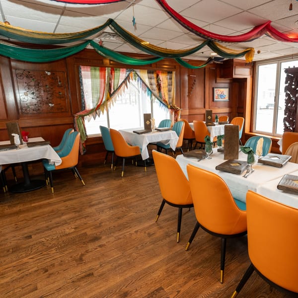 Curry Club dining room with colorful drapes, wooden walls, and tables set with orange and blue chairs.