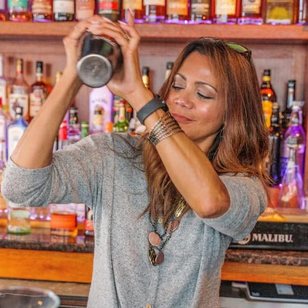 A female bartender with long brown hair shaking a cocktail shaker at Curry Club.