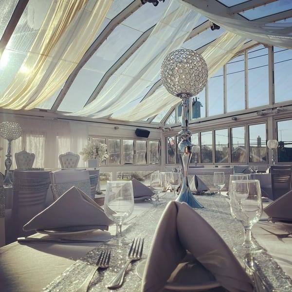 Elegant dining room with white and gold draped ceiling, set tables, and crystal centerpieces.