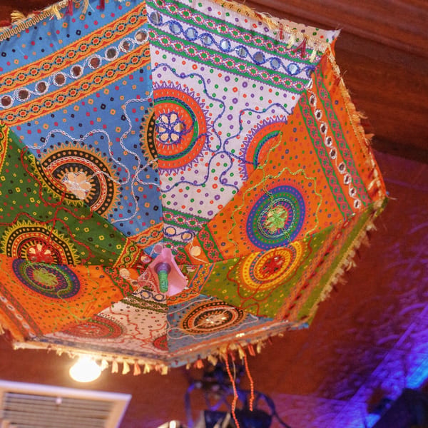 A vibrant, colorful Indian lantern with intricate patterns and mirror work hangs from a ceiling.