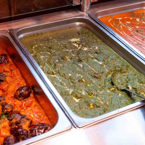 Three buffet trays of Indian curries, including a green spinach dish, a red tomato-based curry, and a creamy orange curry.