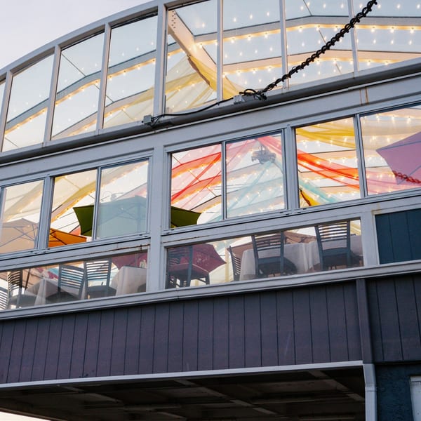 Exterior view of Curry Club's glass-enclosed dining area with colorful fabric and string lights.