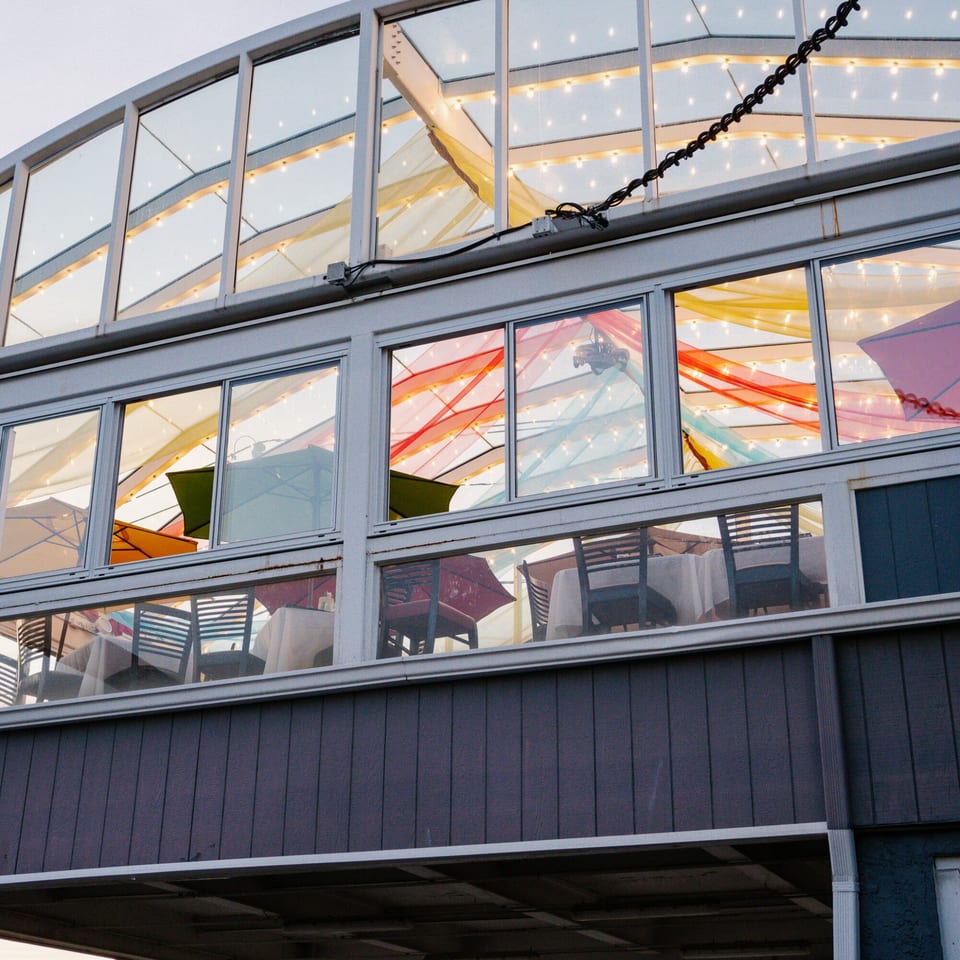 Exterior view of Curry Club's glass-enclosed dining area with colorful fabric and string lights.