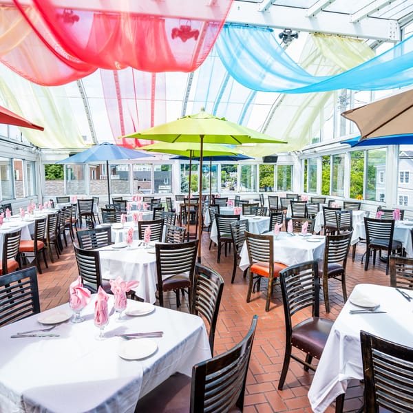 Curry Club's bright, airy dining room with white-clothed tables, dark chairs, and colorful ceiling drapes.