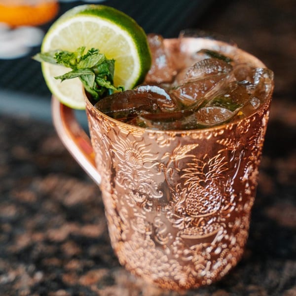 A copper mug filled with ice and a drink, garnished with a lime slice and mint.