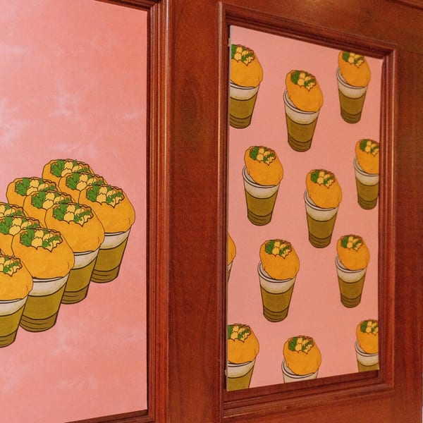 Pink wall art with illustrations of Indian pani puri in cups, framed by dark wood.