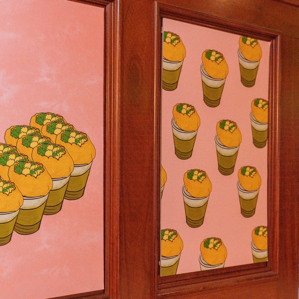 Pink wall art with illustrations of Indian pani puri in cups, framed by dark wood.