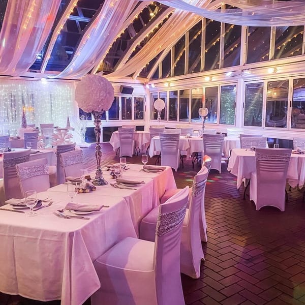 Elegant dining room at Curry Club with white tablecloths, decorated chairs, and draped ceiling lights.