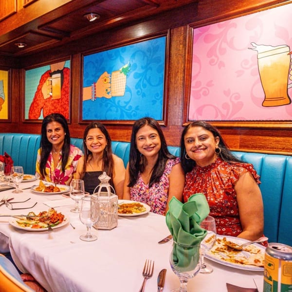 Four women smiling at a table with Indian food and drinks at Curry Club restaurant.