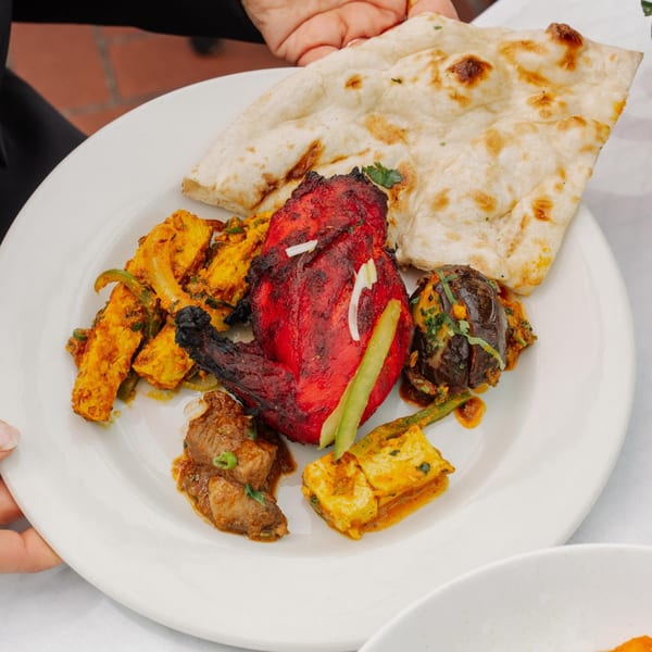 A white plate with various Indian dishes including tandoori chicken, paneer, and naan bread.