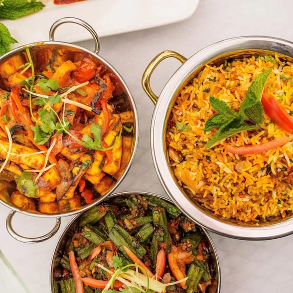 Three Indian dishes: paneer curry, biryani, and okra, served in metal bowls.