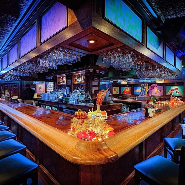 A wide-angle view of the Curry Club bar, featuring a wooden counter, blue bar stools, and hanging glasses.