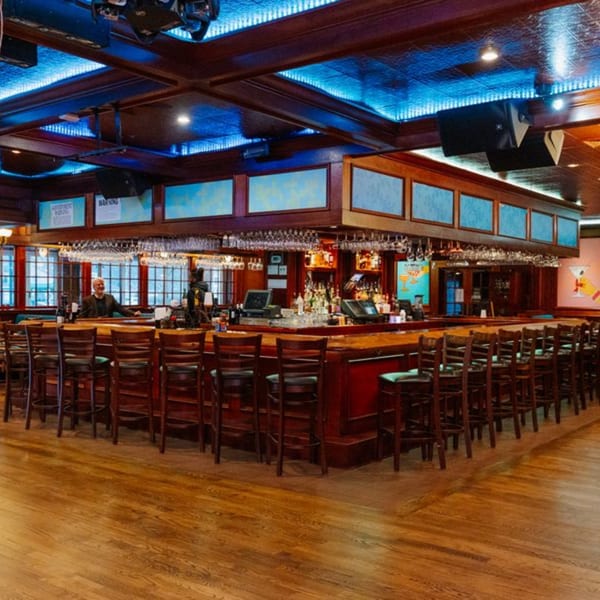 Curry Club's bar area with a long wooden bar, stools, and blue accent lighting on the ceiling.