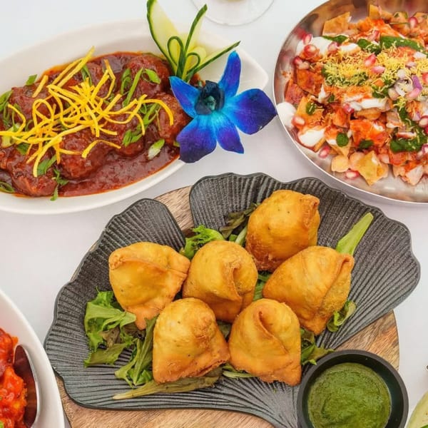 A vibrant Indian feast with samosas, chutney, a curry dish, and a colorful chaat.