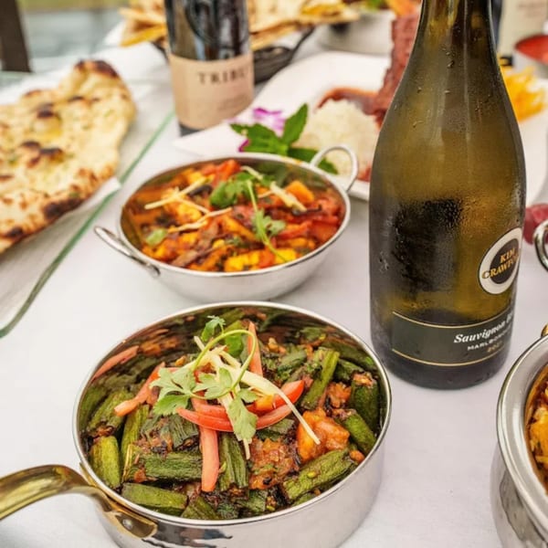 Indian dishes, including okra and paneer curries, naan bread, and a bottle of white wine.