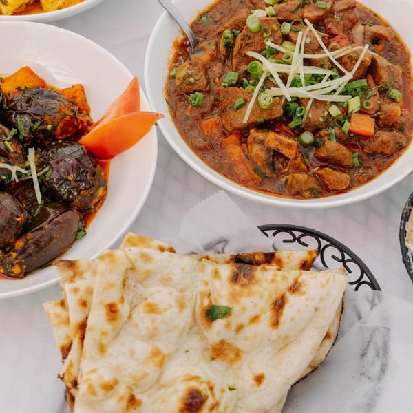 Curry Club's Indian dishes: lamb curry, eggplant bharta, and naan bread on a white tablecloth.