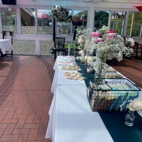 A decorated table with flowers and small gifts, set on a brick patio with large windows.