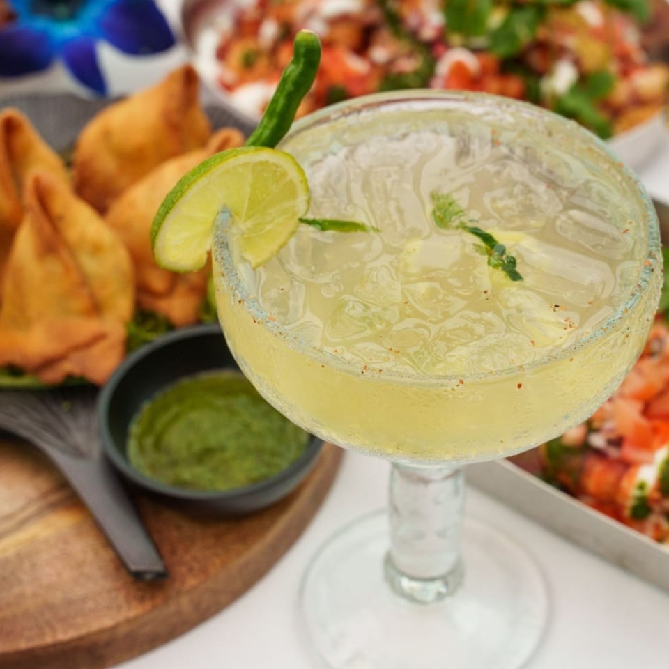 A margarita with a lime wedge and chili salt rim, with Indian samosas and chutney in the background.