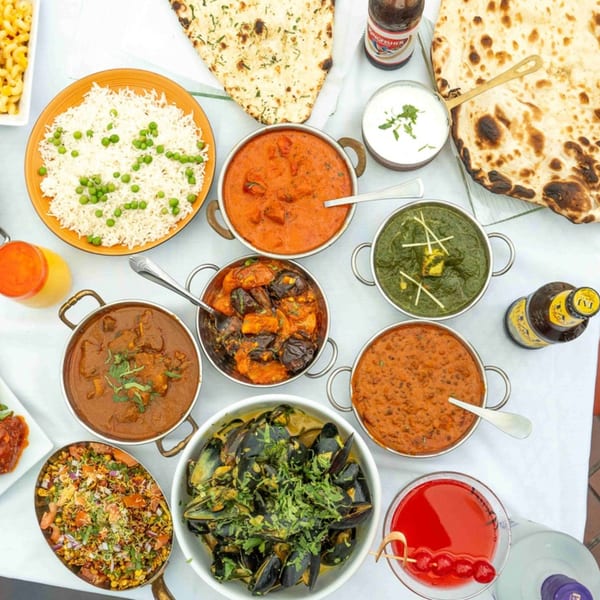 An overhead view of a table laden with various Indian dishes, including curries, rice, naan, and drinks.