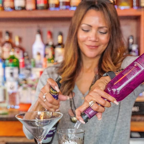 A smiling bartender pours a drink from a purple bottle into a glass at Curry Club.