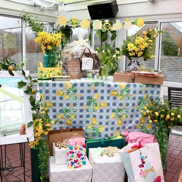 A table with a lemon-patterned tablecloth, decorated with flowers, lemons, and gifts for a bridal shower.