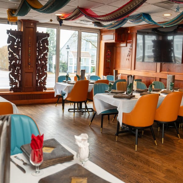 Curry Club dining room with set tables, orange and blue chairs, and decorative Indian textiles.