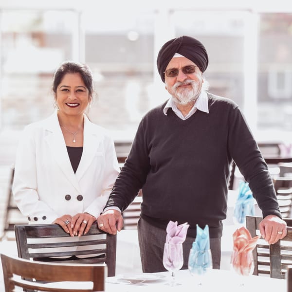 Curry Club owners, a man and woman, smiling behind a dining table with colorful napkins.