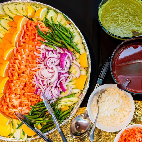A vibrant Indian salad bar with sliced cucumbers, tomatoes, onions, lemons, green chilies, and chutneys.