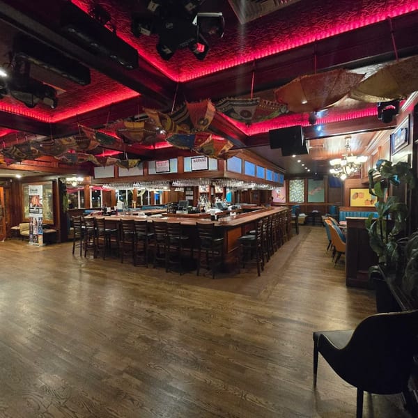 The Curry Club restaurant interior features a large bar, wooden floors, and colorful umbrellas hanging from the ceiling.
