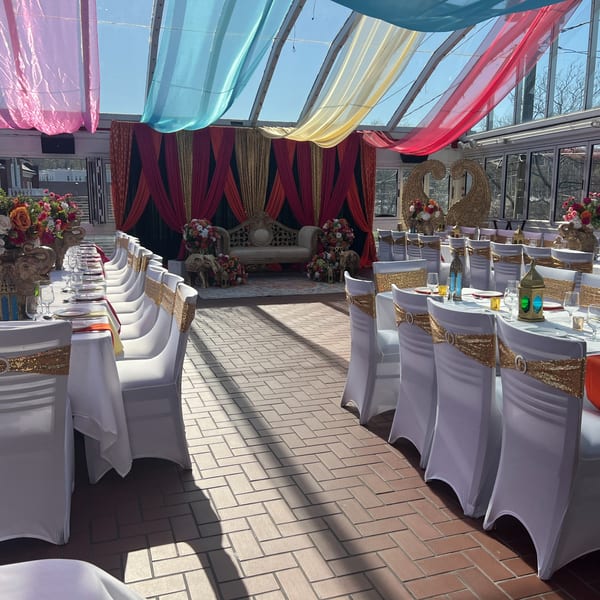 Curry Club's sunlit event space with decorated tables, white chairs, and a stage with a sofa.
