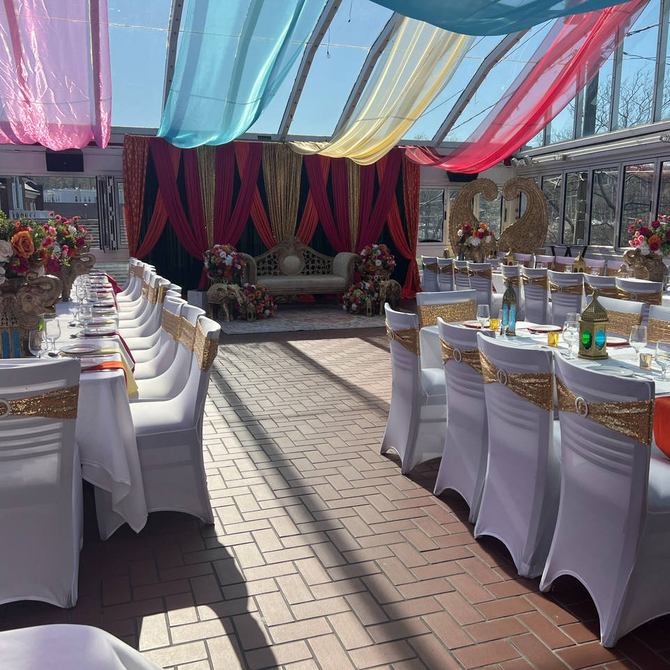 Curry Club's sunlit event space with decorated tables, white chairs, and a stage with a sofa.