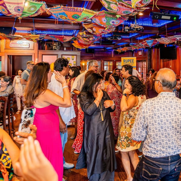 Guests dancing and socializing under colorful, patterned umbrellas at Curry Club Indian restaurant.