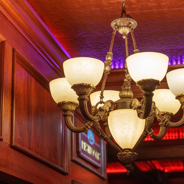 Ornate chandelier with glowing white globes, against a dark wood wall and red-lit ceiling.