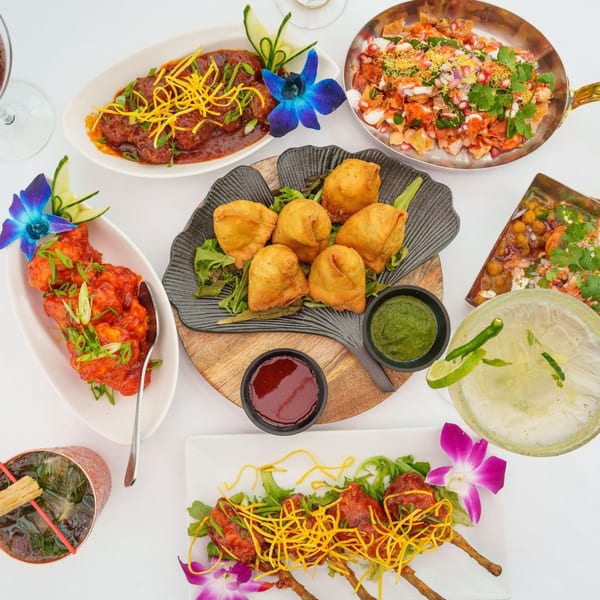 Overhead view of various Indian dishes and cocktails, including samosas, chaat, and chicken lollipops.