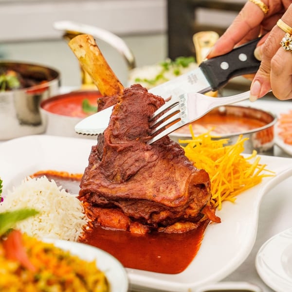 A person cutting into a large lamb shank with rice and shredded carrots on a white plate.