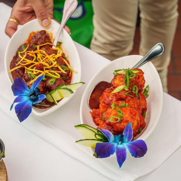 Two bowls of Indian food, one with red sauce and yellow garnish, the other with red sauce and green onions.