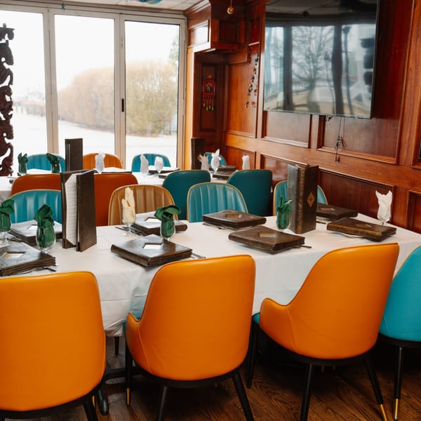 Curry Club dining room with set tables, orange and teal chairs, and large windows.