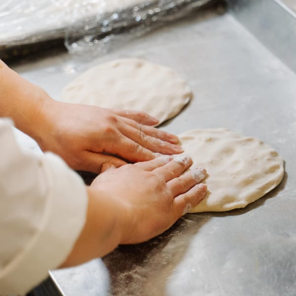 Hands pressing down on two pieces of dough, preparing Indian naan bread.