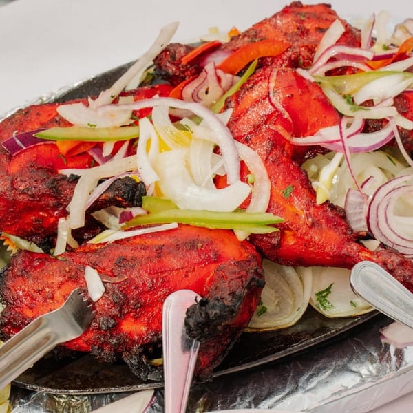 Tandoori chicken, bright red and charred, topped with sliced onions and peppers, served on a sizzling platter.