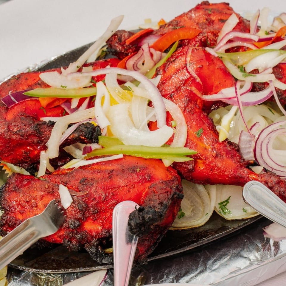 Tandoori chicken, bright red and charred, topped with sliced onions and peppers, served on a sizzling platter.