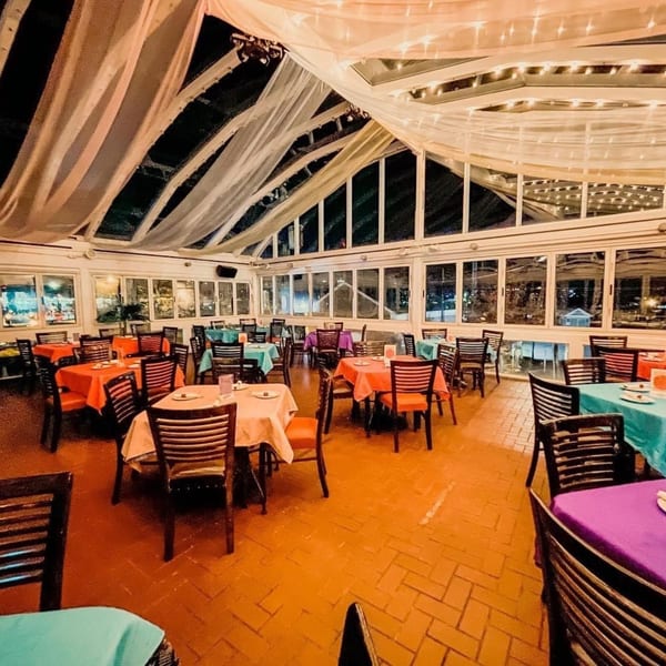 Curry Club's dining room with colorful tablecloths, dark chairs, and a draped, lit ceiling.
