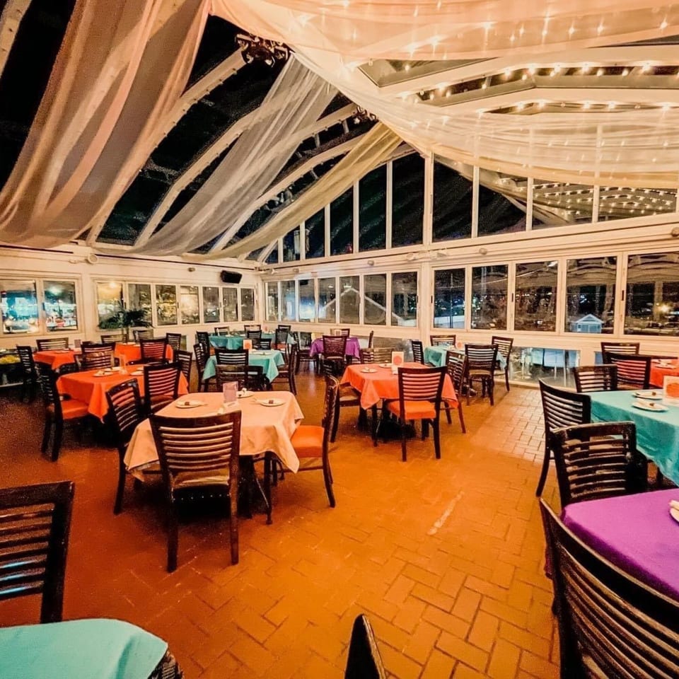 Curry Club's dining room with colorful tablecloths, dark chairs, and a draped, lit ceiling.