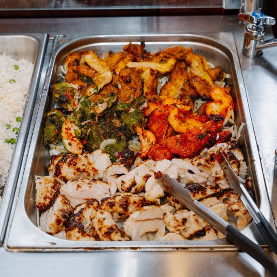 A buffet tray of colorful Indian tandoori chicken, including green, red, and plain varieties, with rice.