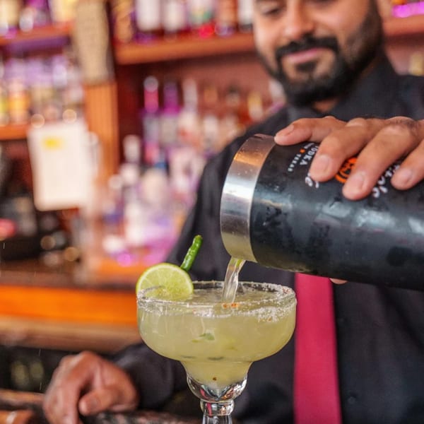 Bartender pouring a margarita with a lime and chili garnish at Curry Club.