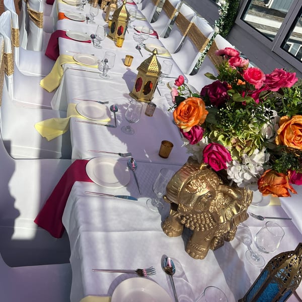 Long dining table set with white tablecloths, colorful napkins, gold lanterns, and floral centerpieces.