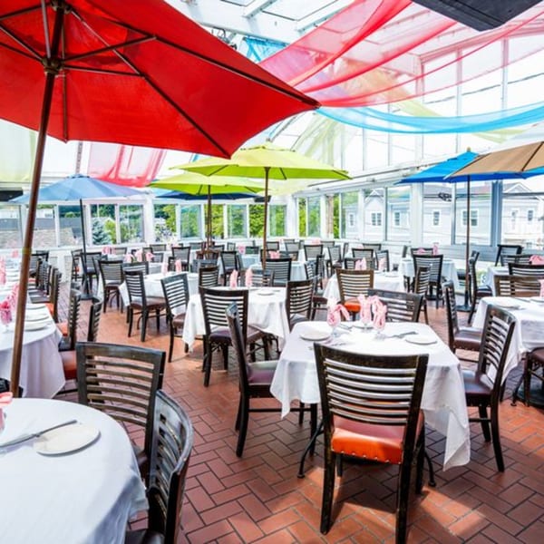 Curry Club's outdoor dining area with tables, chairs, colorful umbrellas, and draped fabric under a glass roof.