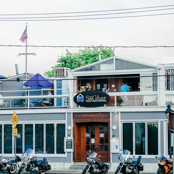 The Curry Club restaurant exterior with a large sign, outdoor seating, and motorcycles parked in front.