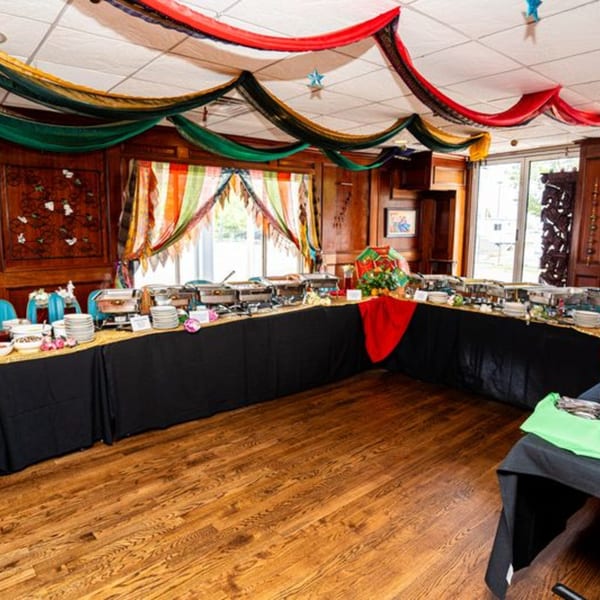 An Indian buffet setup with chafing dishes, plates, and colorful fabric decorations on the ceiling.