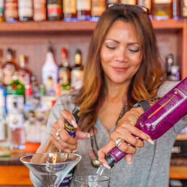 A smiling bartender pours a drink from a purple bottle into a glass at Curry Club.